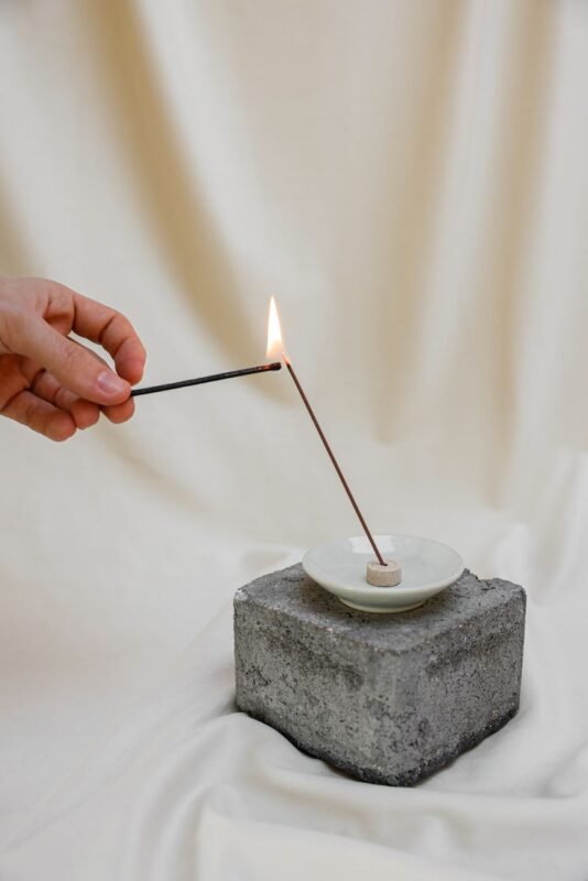 person lighting an incense stick on white candle holder
